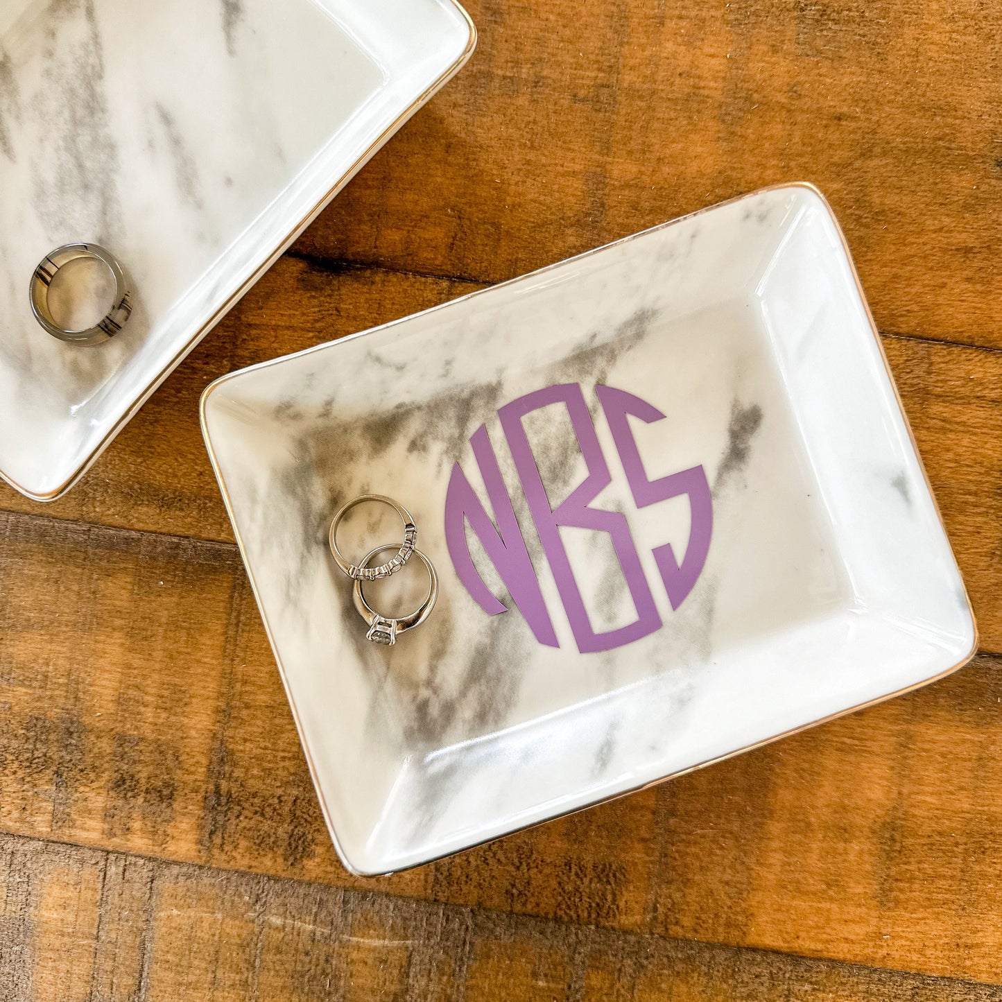 Marble-patterned jewelry dish with 'NIBS' monogram on a wooden surface