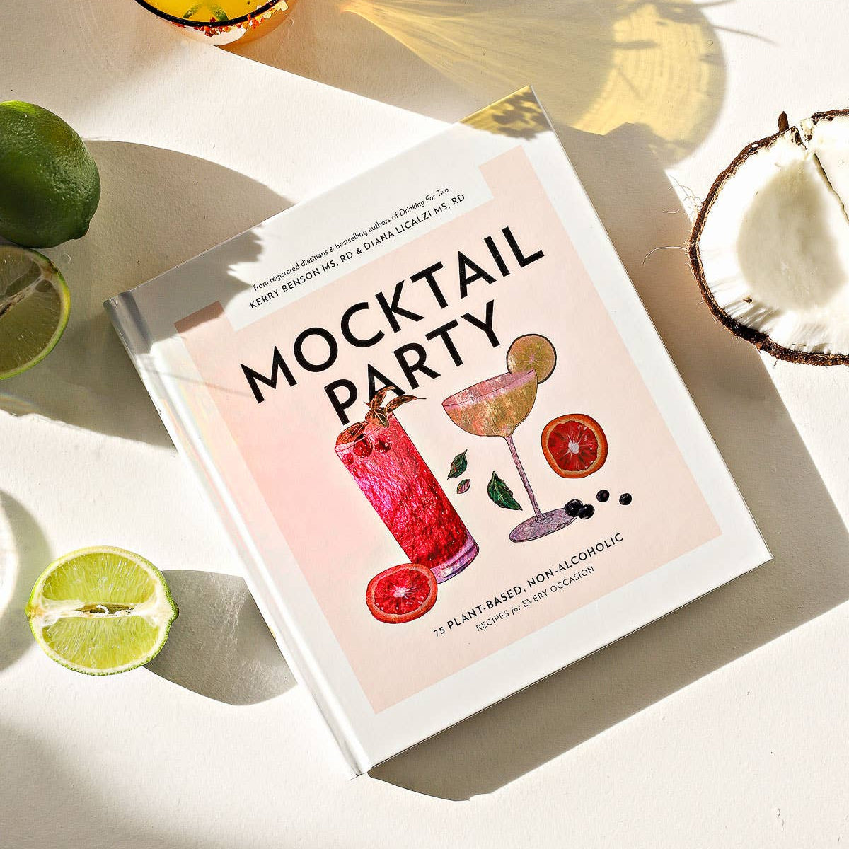 Book titled 'Mocktail Party' with cocktail illustrations on a light surface with ingredients.